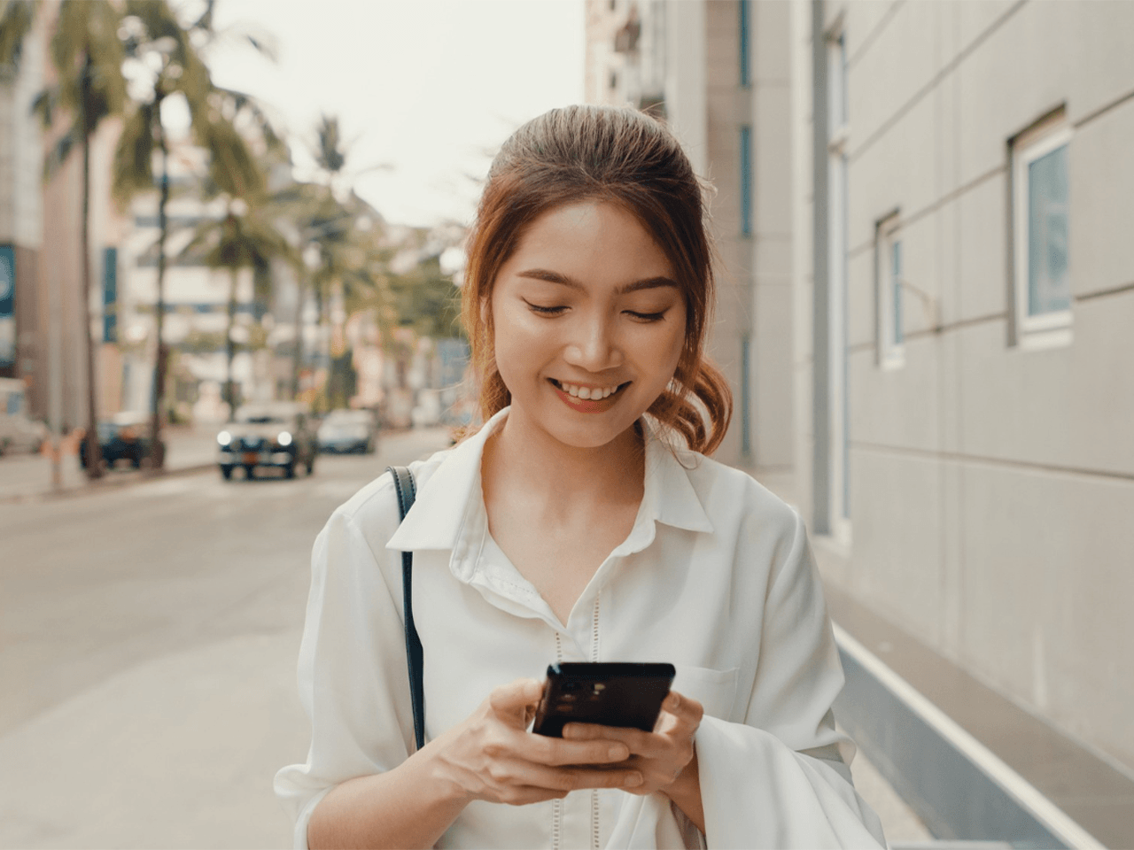 Asian woman walking along a city street while looking at her mobile phone.